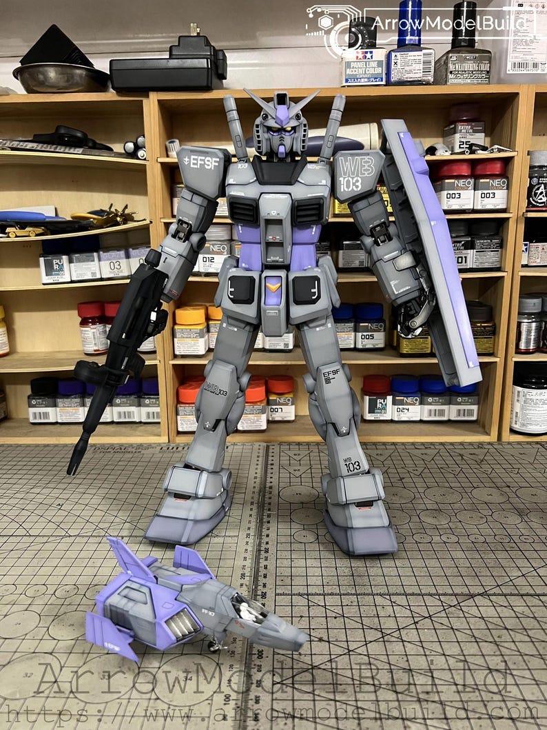 May include: A detailed model of a gray and purple robot with a matching aircraft. The robot has the text "EFSF" and "WB 103" printed on it. The aircraft is gray and purple with the text "ArrowModelBuild" on the bottom.