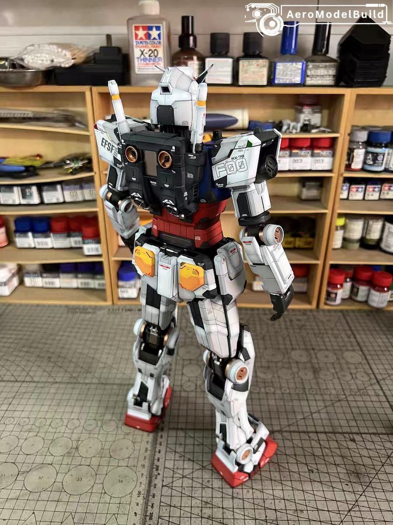 May include: A detailed model of a white, black, and red robot with orange and blue accents. The model has intricate paneling and mechanical details, with the text "EFSF" and "F03" visible. The robot is posed on a gray surface.