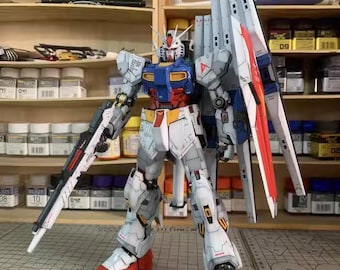 May include: A detailed model of a Gundam robot, primarily white, blue, red, and yellow. The model has a large weapon and wings. The text "ArrowModelBuild" is visible at the top and bottom of the image.