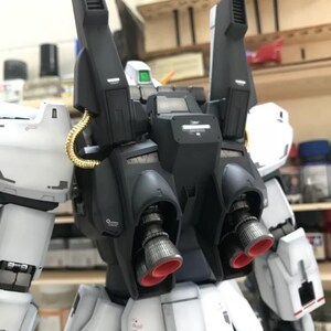 Op de afbeelding: Gedetailleerd model van een witte en zwarte robot met rode accenten op de stuwraketten. De robot heeft een complex ontwerp met meerdere componenten, waaronder grote zwarte boosters en goudkleurige buizen. Het AeroModelBuild-logo is zichtbaar.