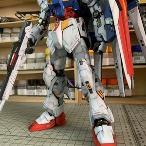 K&ouml;nnte beinhalten: Detailliertes Modell eines Roboters, haupts&auml;chlich wei&szlig;, blau, rot und grau. Der Roboter h&auml;lt eine gro&szlig;e Waffe und hat einen Schild auf dem R&uuml;cken. Das Modell steht auf einer Rasteroberfl&auml;che, mit Regalen und Zubeh&ouml;r im Hintergrund.