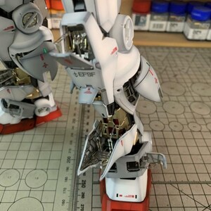 K&ouml;nnte beinhalten: Ein detailliertes, teilweise zusammengebautes Modell eines Roboters mit wei&szlig;en, grauen, roten und goldenen Akzenten. Das Modell weist komplizierte mechanische Details auf, einschlie&szlig;lich sichtbarer interner Komponenten und dem Text "EFSF". Ein Lineal ist im Hintergrund sichtbar.