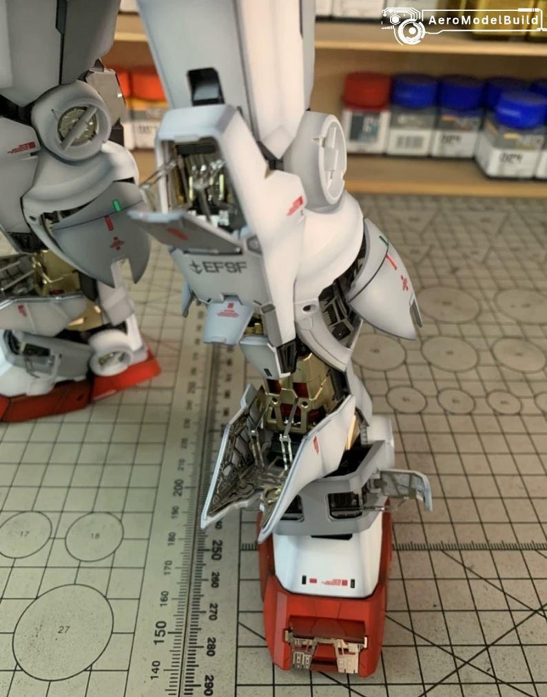 K&ouml;nnte beinhalten: Ein detailliertes, teilweise zusammengebautes Modell eines Roboters mit wei&szlig;en, grauen, roten und goldenen Akzenten. Das Modell weist komplizierte mechanische Details auf, einschlie&szlig;lich sichtbarer interner Komponenten und dem Text "EFSF". Ein Lineal ist im Hintergrund sichtbar.