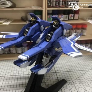 May include: A blue and white model airplane with a detailed design. The model has a sleek, aerodynamic shape with wings and a tail. The model is on a black stand. The AeroModelBuild logo is in the top right corner.
