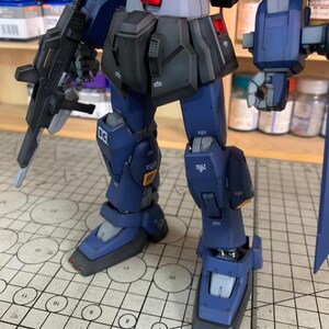 May include: A detailed, partially assembled model robot with a dark blue and black color scheme. The robot has a gun, and the text "03" is visible on the leg. The image also includes the text "Arrow ModelBuild" and a website address.
