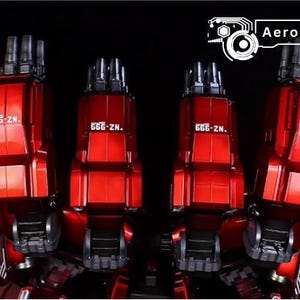 May include: Close-up of a red model robot's legs and feet, with the text "666-ZN." visible on each leg. The model has a metallic finish and is set against a black background. The AeroModelBuild logo is in the top right corner.