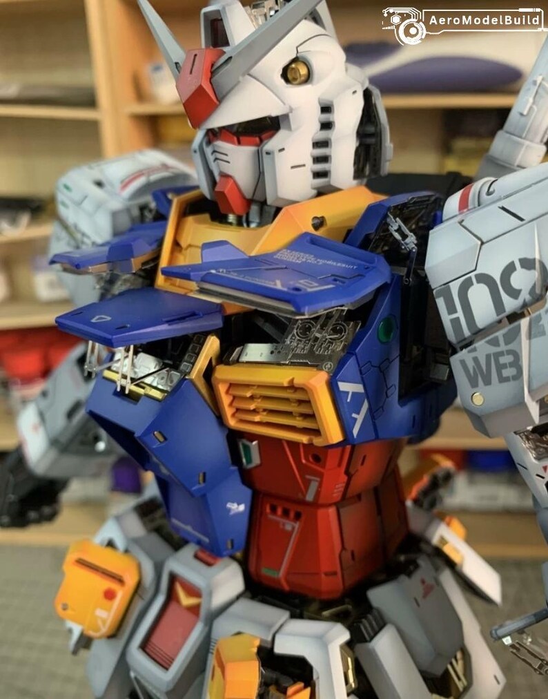 K&ouml;nnte beinhalten: Detailliertes Modell eines Gundam-Roboters mit einem wei&szlig;en Kopf mit roten und gelben Akzenten. Der Roboter-K&ouml;rper besteht aus blauen, roten, gelben und grauen Paneelen mit komplizierten mechanischen Details. Der Text "AeroModelBuild" ist enthalten.