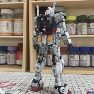 以下が含まれることがあります： 赤、青、黄色のアクセントが付いた、主に白のガンダムロボットの詳細なモデル。モデルは背面から見ており、複雑な機械的詳細が明らかになっています。モデルはグリッド表面に配置されています。