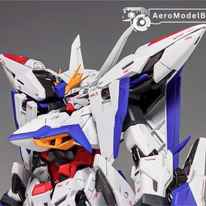 Puede incluir: Primer plano de un modelo de robot blanco, azul, rojo y amarillo. El modelo tiene detalles intrincados, &aacute;ngulos agudos y un dise&ntilde;o futurista. El texto "AeroModelBuild" es visible en la esquina superior derecha.