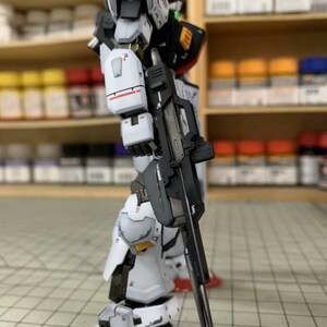 Pode incluir: Um modelo detalhado de um rob&ocirc; branco, preto e cinza com detalhes vermelhos, segurando um rifle preto. O modelo tem detalhes intrincados e est&aacute; posicionado em uma superf&iacute;cie quadriculada. O logotipo AeroModelBuild &eacute; vis&iacute;vel no fundo.