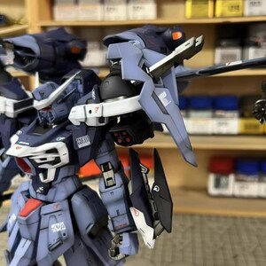 May include: A detailed, partially assembled model kit of a futuristic robot, primarily in shades of blue and gray with red and white accents. The model features intricate mechanical details, including articulated limbs and various weapon-like attachments. The AeroModelBuild logo is visible.