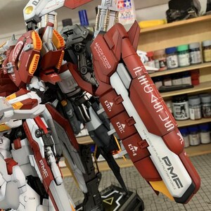 Puede incluir: Modelo detallado de un robot con armadura roja, blanca y gris. El modelo tiene m&uacute;ltiples partes articuladas y est&aacute; etiquetado con texto que incluye "MAGX-0033" y "PME". El modelo est&aacute; sobre un soporte negro, con un acento amarillo y blanco.