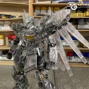 May include: A transparent plastic robot model with articulated limbs and wings. The robot features a detailed design with visible internal components. The model is posed dynamically, highlighting its intricate construction. The background includes shelves with paint supplies.