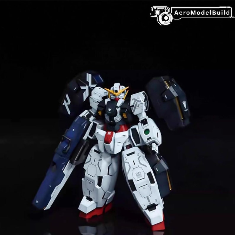 May include: A white and blue model robot with red and yellow accents. The robot has large shoulder armor and a detailed design. The image is set against a dark background.
