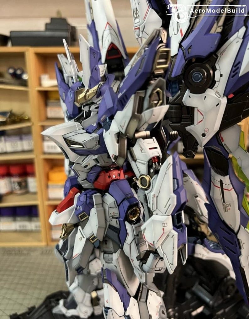 May include: A highly detailed model robot, predominantly white, purple, red, and gold. The design incorporates intricate mechanical elements and sharp angles, giving a futuristic appearance. The background is blurred, focusing attention on the model's complex structure.