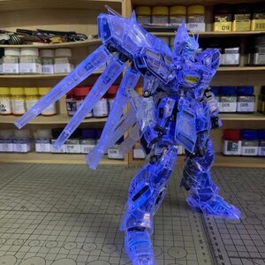 May include: A transparent blue model robot with illuminated wings and body parts. The robot is standing on a gray surface with a ruler. The background includes shelves with various containers and the AeroModelBuild logo.