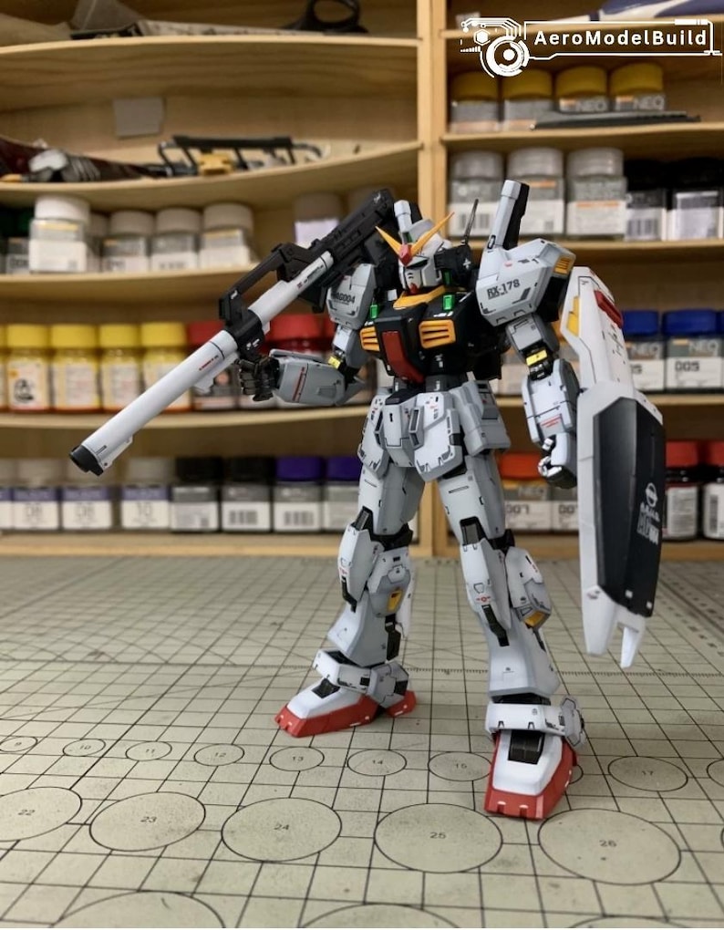Pode incluir: Modelo detalhado de um rob&ocirc; Gundam, predominantemente branco com detalhes em preto, vermelho e amarelo. O rob&ocirc; est&aacute; segurando um grande rifle branco e preto e tem um escudo no bra&ccedil;o esquerdo. O modelo est&aacute; em uma superf&iacute;cie quadriculada.