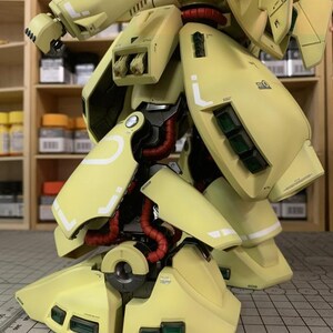 May include: A detailed, close-up view of a yellow model robot's lower body. The model features articulated legs, with red tubing and white accent lines. The image includes the text "ArrowModelBuild" in the upper right corner.