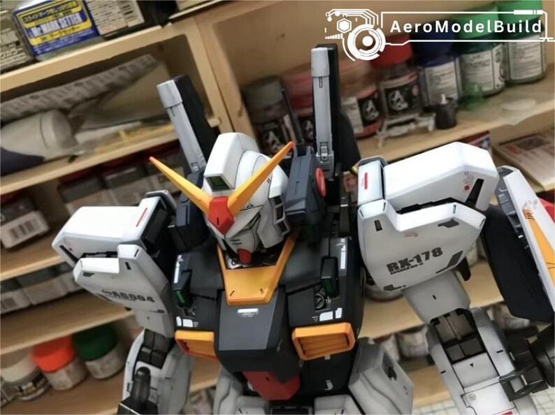 Op de afbeelding: Een gedetailleerde modelbouwkit van een Gundam-robot, met een wit, zwart, oranje en rood kleurenschema. Het model heeft ingewikkelde details, inclusief de tekst "RX-178" en "AeroModelBuild" op de afbeelding.