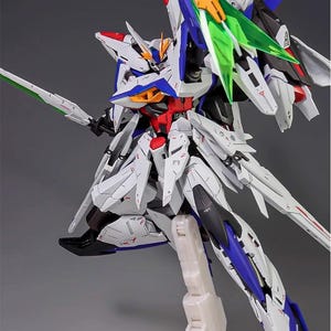 Puede incluir: Modelo detallado de un robot futurista, predominantemente blanco con detalles azules, rojos y amarillos. Cuenta con grandes alas, una espada y est&aacute; montado sobre un soporte. El logotipo de AeroModelBuild es visible.