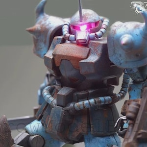 May include: A detailed model of a robot with a weathered, battle-worn appearance. The robot is primarily blue with rust-colored accents, and features a glowing pink light in its head. It has a shield and a sword, suggesting a combat theme.