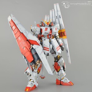 May include: A detailed model robot, predominantly white with red and yellow detailing. The model features large wings and is set against a grey backdrop. The intricate design suggests a collectible item.