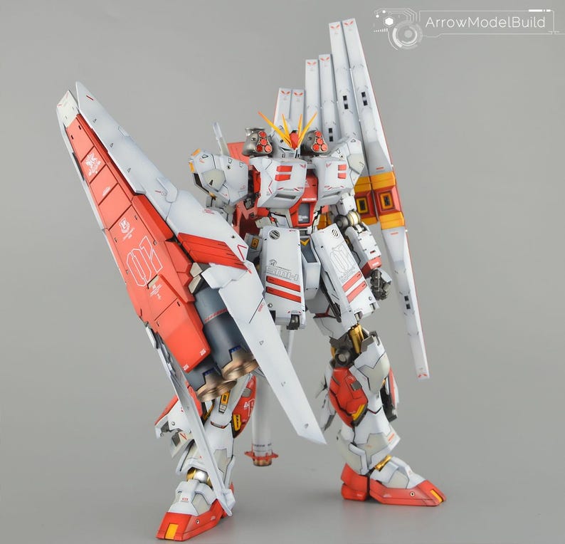 May include: A detailed model robot, predominantly white with red and yellow detailing. The model features large wings and is set against a grey backdrop. The intricate design suggests a collectible item.