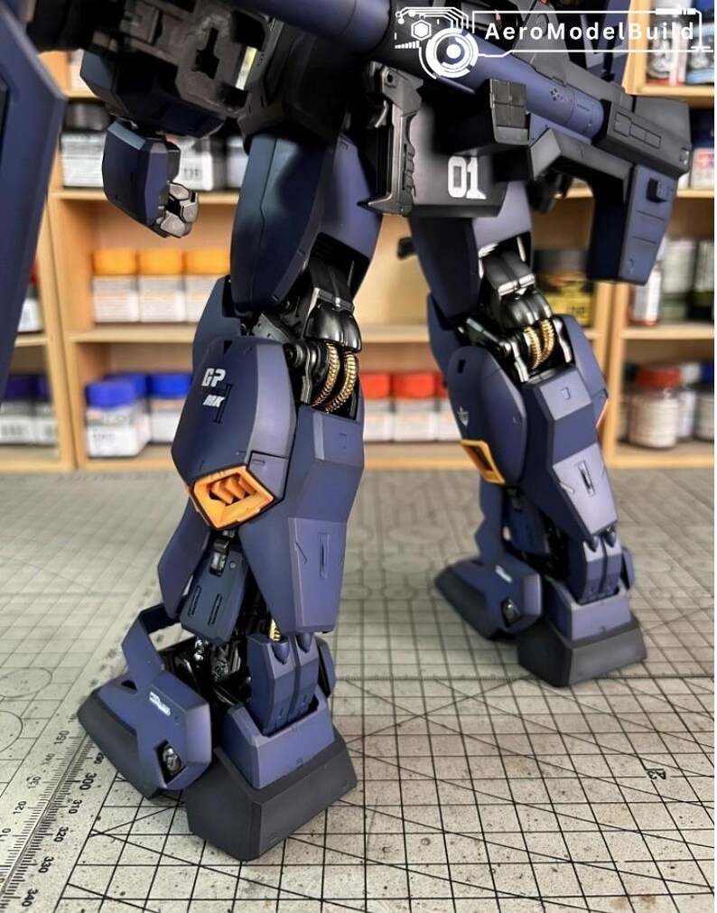 Pu&ograve; includere: Primo piano delle gambe e del busto inferiore di un modello di robot blu scuro e nero. Il modello presenta dettagli dorati e arancioni, con il numero "01" visibile. L'immagine mette in risalto gli intricati dettagli del modello.