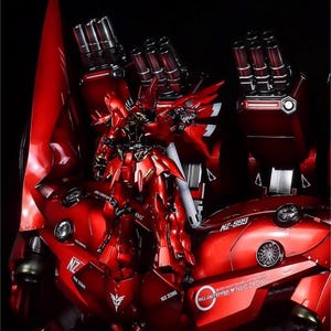 May include: A detailed, red model of a mecha robot, featuring intricate designs and multiple weapon systems. The model has a glossy finish and is set against a dark background. The text "NZ-999" and "Neo Zeong" are visible.