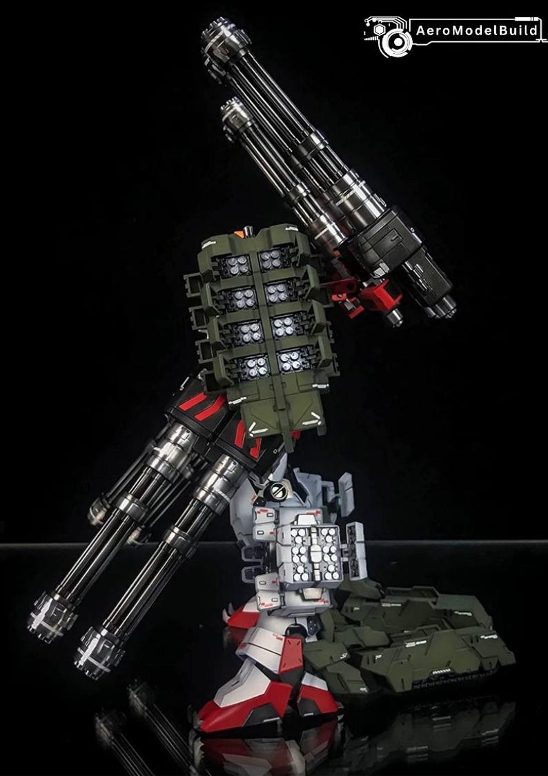 K&ouml;nnte beinhalten: Ein detaillierter Roboter-Modellbausatz in den Farben Wei&szlig;, Rot und Olivgr&uuml;n. Die Figur ist mit zwei gro&szlig;en Gatling-Gesch&uuml;tzen mit mehreren L&auml;ufen und mehreren Raketenwerfern ausgestattet. Der Text AeroModelBuild ist in der Ecke zu sehen.