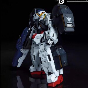 May include: A detailed model of a Gundam robot, primarily white with accents of red, blue, and black. The robot has a complex design with multiple panels and articulated joints. The image includes the text "AeroModelBuild".