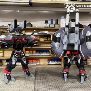 May include: Two detailed model robots, one facing forward and the other backward, with a workshop background. The robots are primarily black, red, and gray, with intricate designs and mechanical features. The AeroModelBuild logo is visible.