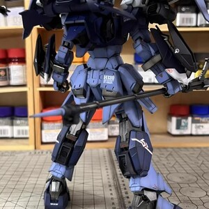 May include: A detailed, assembled model of a robotic figure in shades of blue and black. The model features intricate mechanical details, including wings, weapons, and the text "H130". The figure is posed on a surface with a ruler.