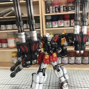 K&ouml;nnte beinhalten: Detailliertes Modell eines Roboters mit roten, wei&szlig;en, schwarzen und gelben Akzenten. Der Roboter ist mit mehreren Kanonenl&auml;ufen an jeder Schulter ausgestattet. Das Modell steht auf einer Rasteroberfl&auml;che, mit Farbt&ouml;pfen im Hintergrund.