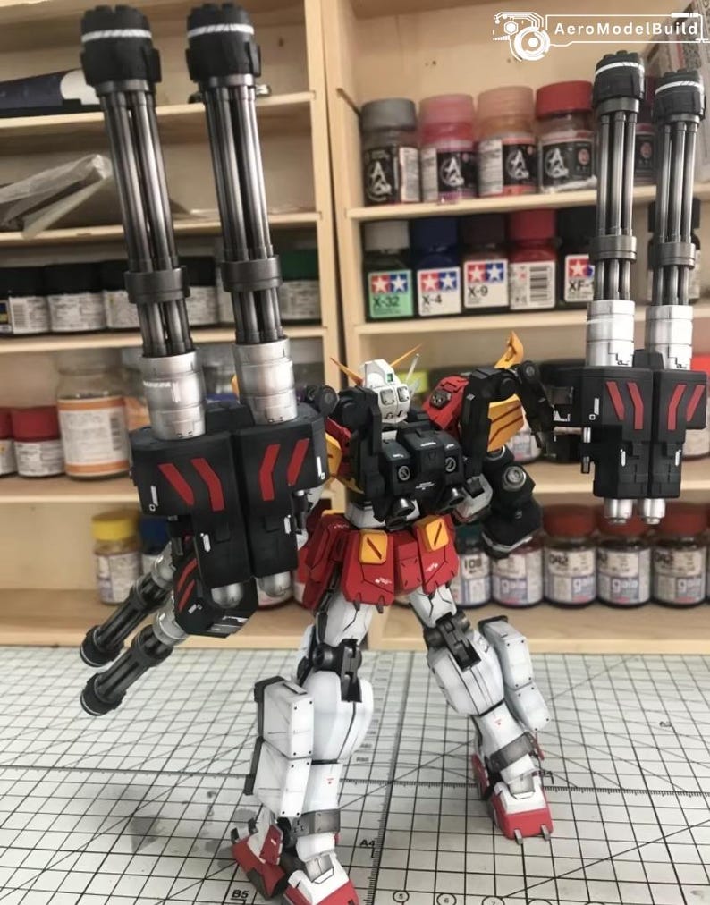 K&ouml;nnte beinhalten: Detailliertes Modell eines Roboters mit roten, wei&szlig;en, schwarzen und gelben Akzenten. Der Roboter ist mit mehreren Kanonenl&auml;ufen an jeder Schulter ausgestattet. Das Modell steht auf einer Rasteroberfl&auml;che, mit Farbt&ouml;pfen im Hintergrund.