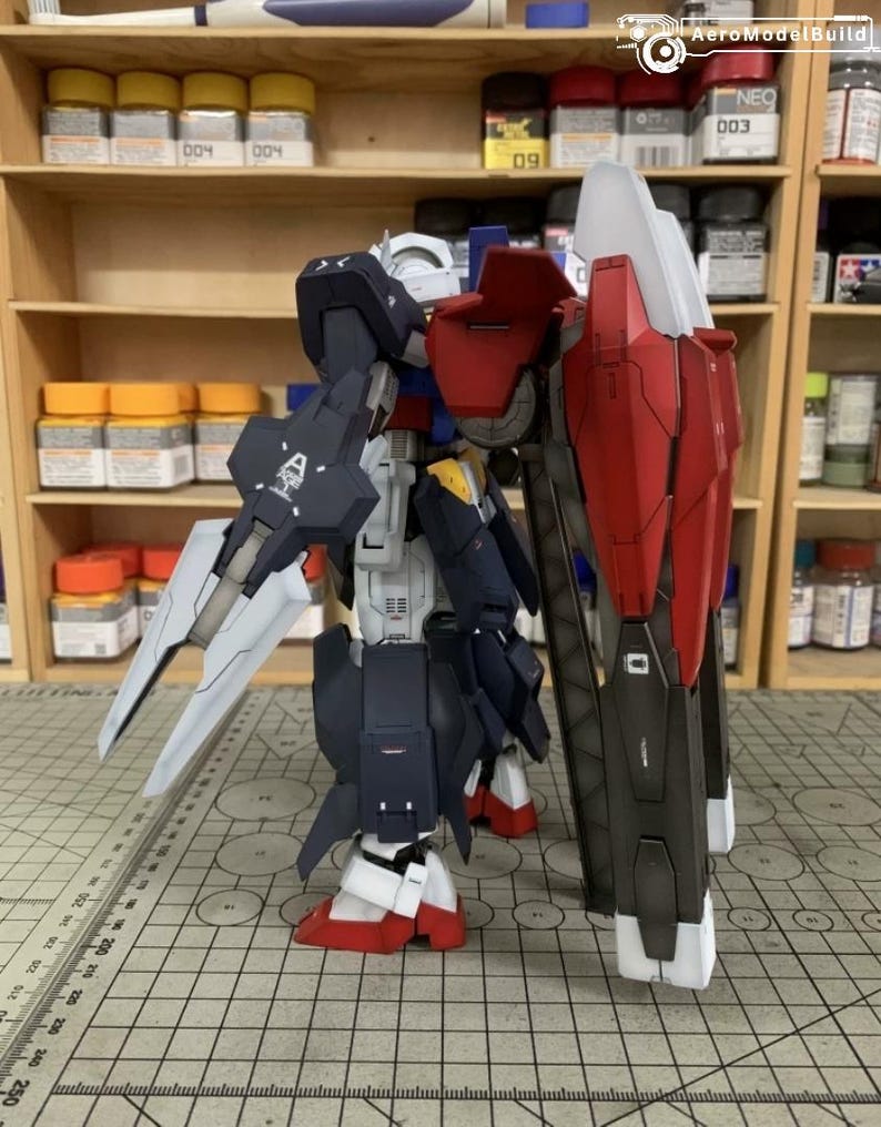 Puede incluir: Modelo detallado de un robot, con una combinaci&oacute;n de colores azul marino, rojo, blanco y gris. El robot tiene un escudo grande y una espada. El modelo est&aacute; colocado sobre una superficie con un patr&oacute;n de cuadr&iacute;cula, lo que sugiere un proyecto de modelismo.