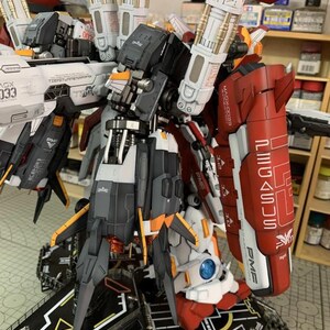 Puede incluir: Un detallado kit de modelo de robot mec&aacute;nico, con una combinaci&oacute;n de colores rojo, blanco, gris y naranja. El modelo tiene intrincados detalles mec&aacute;nicos, incluyendo m&uacute;ltiples paneles, articulaciones y armas. La base es una plataforma negra con marcas blancas y amarillas. El texto "MAGX-0033" es visible.
