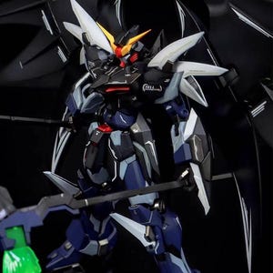 Puede incluir: Modelo detallado de un robot Gundam, principalmente en azul oscuro y negro, con detalles blancos y amarillos. El robot tiene grandes alas y sostiene un arma. El logotipo de AeroModelBuild es visible en la esquina superior derecha.