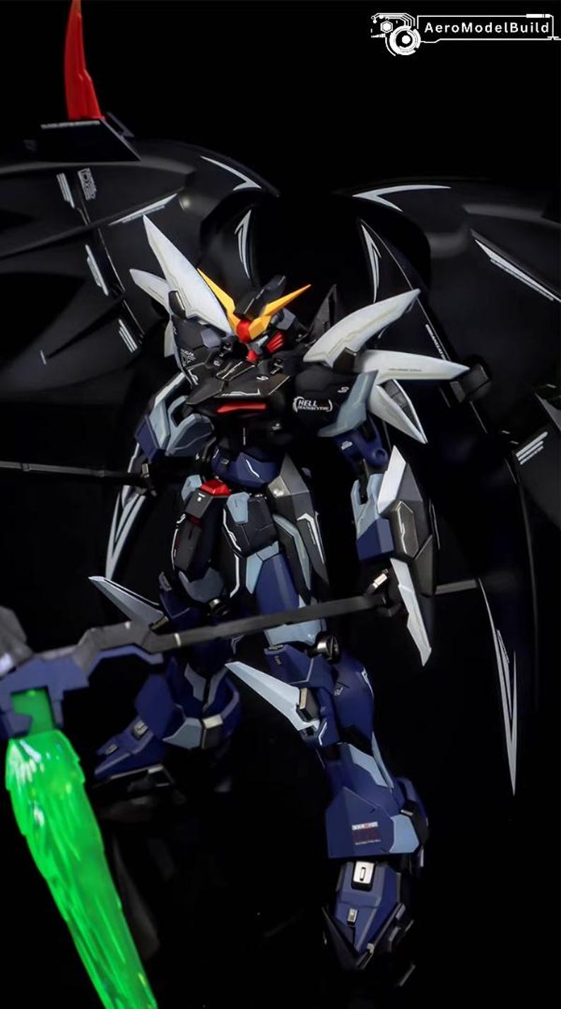 Puede incluir: Modelo detallado de un robot Gundam, principalmente en azul oscuro y negro, con detalles blancos y amarillos. El robot tiene grandes alas y sostiene un arma. El logotipo de AeroModelBuild es visible en la esquina superior derecha.