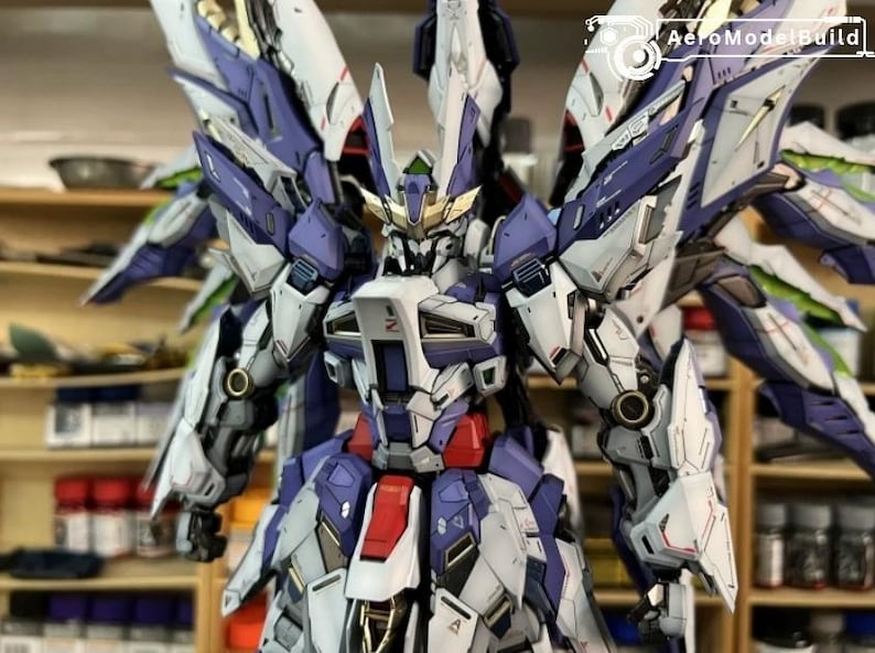 May include: A detailed model robot, predominantly white, purple, and red. It features large wings and intricate mechanical details. The model is set against a blurred background of shelves with paint bottles.