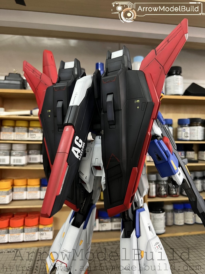 May include: A detailed model kit of a mecha robot, featuring a combination of black, red, white, and blue panels. The model has articulated wings and intricate detailing, with the text "AG ALUCIORE" visible on one of the panels. The model is partially assembled.
