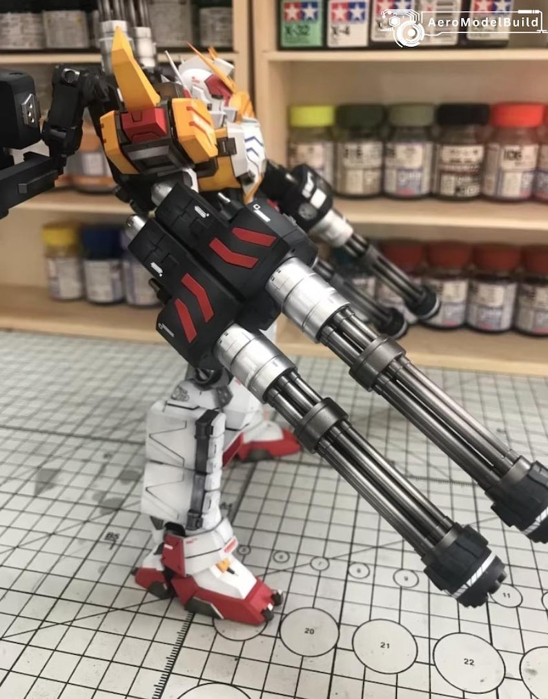 K&ouml;nnte beinhalten: Detailliertes Modell eines Gundam-Roboters mit einer Farbgebung aus Wei&szlig;, Rot, Gelb und Schwarz. Der Roboter ist mit gro&szlig;en, mehrl&auml;ufigen Kanonen ausgestattet und steht auf einer Rasteroberfl&auml;che, die komplizierte mechanische Details zeigt.