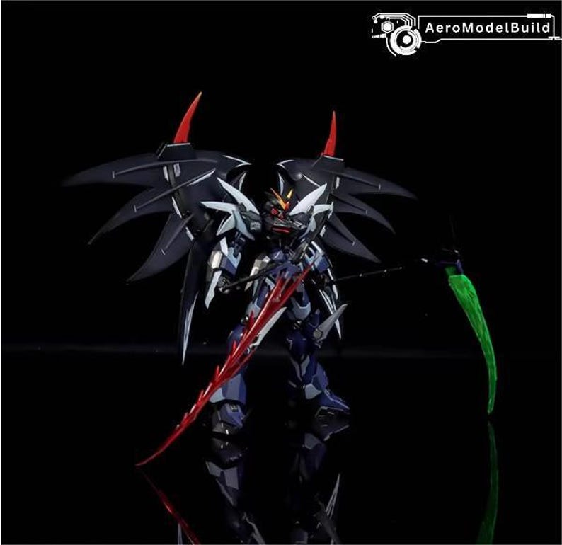 Puede incluir: Logotipo de AeroModelBuild. Modelo detallado de un robot azul oscuro y plateado con grandes alas negras y detalles rojos. El robot sostiene una espada roja y un arma verde en forma de guada&ntilde;a. El fondo es negro.