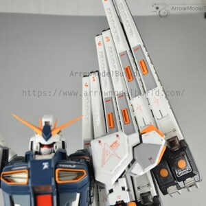 May include: A detailed model kit of a Gundam robot, featuring a white, navy blue, and orange color scheme. The model has intricate paneling and markings, with text visible on the white panels. The robot's head has orange antennae.