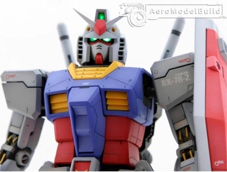 May include: A detailed model of a Gundam robot, featuring a color scheme of blue, red, yellow, and white. The robot has a detailed head with green glowing eyes and a red crest. The model includes a shield and is set against a white background.