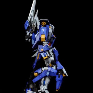 May include: A detailed model kit of a robot figure, predominantly blue, white, and yellow, with a large blade weapon. The figure is posed dynamically against a black background, showcasing its intricate design and articulation. The text "AeroModelBuild" is in the upper right corner.