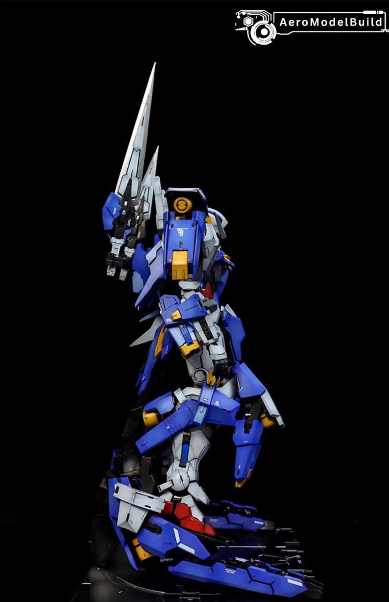 May include: A detailed model kit of a robot figure, predominantly blue, white, and yellow, with a large blade weapon. The figure is posed dynamically against a black background, showcasing its intricate design and articulation. The text "AeroModelBuild" is in the upper right corner.