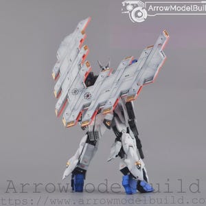May include: A white and grey model robot with large, angled wings and orange and gold accents. The robot has blue feet and is set against a grey background. The text "ArrowModelBuild" is visible.