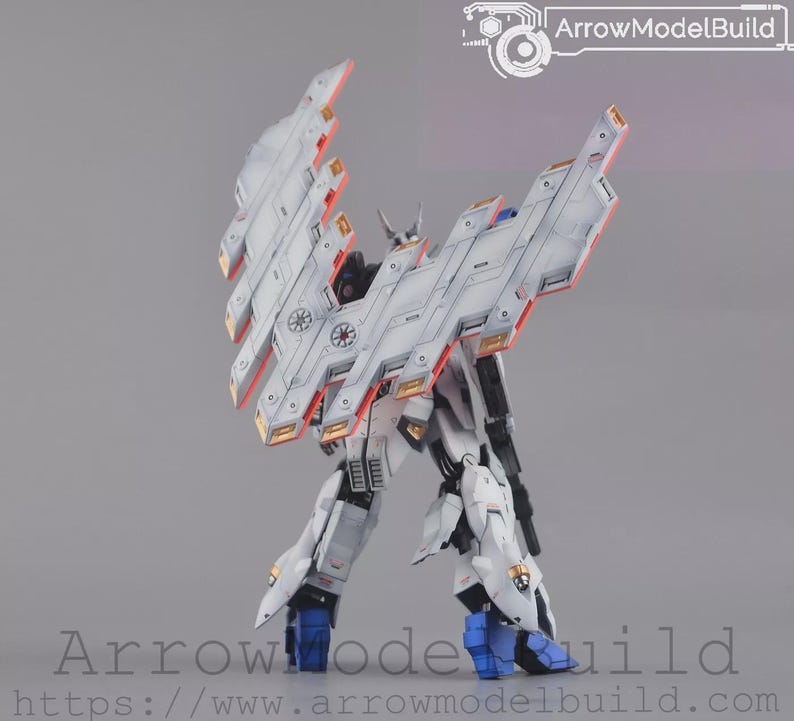 May include: A white and grey model robot with large, angled wings and orange and gold accents. The robot has blue feet and is set against a grey background. The text "ArrowModelBuild" is visible.