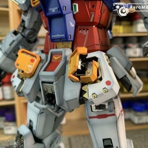 K&ouml;nnte beinhalten: Ein detailliertes, teilweise zusammengebautes Modell eines Roboters mit einem Farbschema aus Rot, Blau, Grau und Gelb. Der Torso und die Beine des Roboters sind sichtbar und zeigen komplizierte mechanische Details und Linien. Der Text "AeroModelBuild" ist sichtbar.